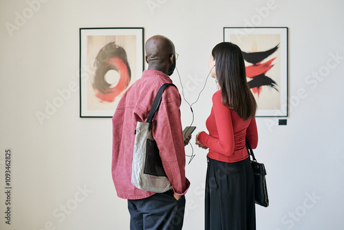 Εκτύπωση καμβά Two individuals in an art gallery observing framed paintings on a white wall while engaged in conversation