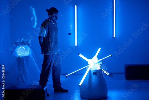 Individual admiring contemporary art installation in dimly lit room with blue lights ambient. Modern sculpture illuminated by LED lights forming a star-like pattern photo