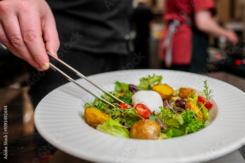 A close-up of a chef’s hand garnishing a gourmet salad with tweezers, highlighting the fresh ingredients and vibrant colors. Perfect for culinary, food styling, and gourmet cuisine themes.