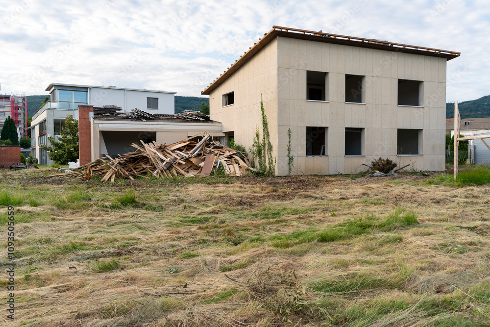 Teardown house with a pile of wooden boards already removed from the core of the house lying in front of it. Old cement asbestos that were removed lying on the roof. Teardown house with a pile of wooden boards already removed from the core of the house lying in front of it. Old cement asbestos that were removed lying on the roof.