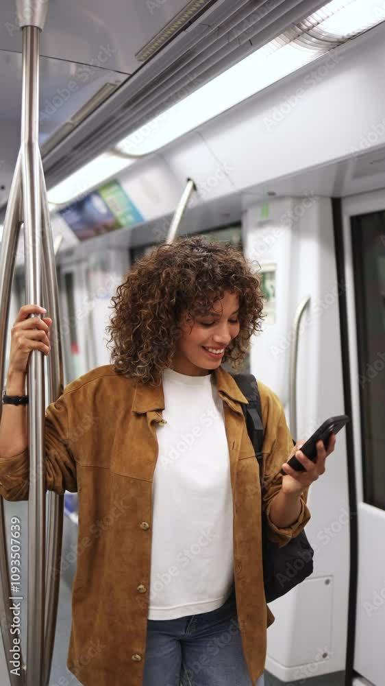 Young woman stands on a subway train, holding a smartphone and browsing social media with a smile. Woman browsing social media on subway in slow motion Young woman stands on a subway train, holding a smartphone and browsing social media with a smile. Woman browsing social media on subway in slow motion