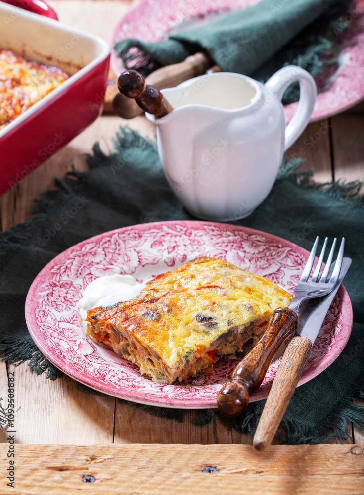 Oven baked omelette with vegetables served with sour cream on wooden background.