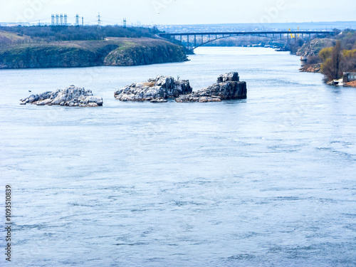 Dnipro river splitting around Khortytsia island and huge rocks south of DniproHES dam in city of Zaporizhzhia, Ukraine. Backlit shot.