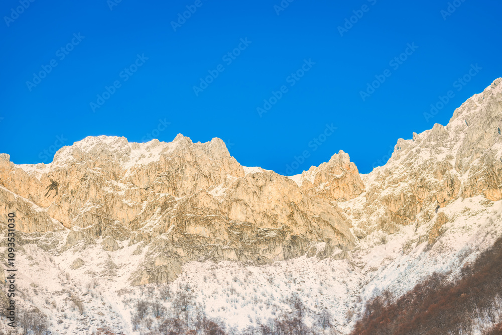 A stunning view of a snow-covered mountain ridge under a vibrant blue sky. The rugged peaks are bathed in warm sunlight, highlighting the natural texture and grandeur of the landscape. A stunning view of a snow-covered mountain ridge under a vibrant blue sky. The rugged peaks are bathed in warm sunlight, highlighting the natural texture and grandeur of the landscape.