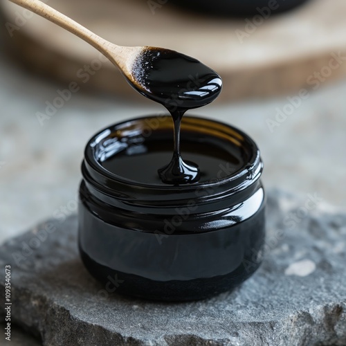 Black shilajit honey drips from spoon into jar. Natural stone background. Healthy superfood. Premium quality product photo. Natural light. Organic product. Health, wellness. Natural remedy. photo