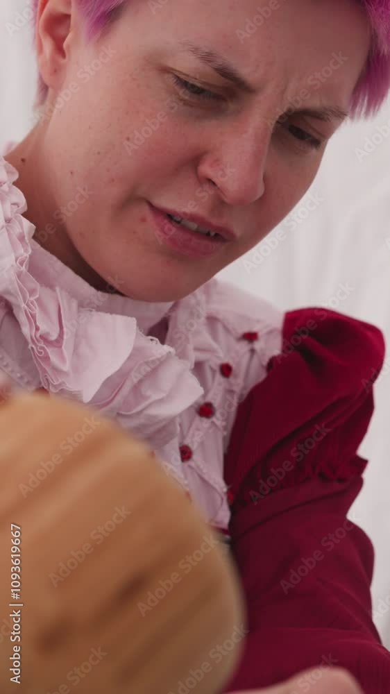 Witch with short bright pink hair pours out ingredient to make potion. Medieval woman in burgundy dress prepares drink with magical properties closeup Witch with short bright pink hair pours out ingredient to make potion. Medieval woman in burgundy dress prepares drink with magical properties closeup