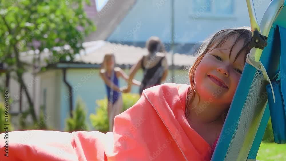 A little girl in a wet swimsuit is sitting in the beach chair wrapped in a cozy towel blanket . High quality 4k footage A little girl in a wet swimsuit is sitting in the beach chair wrapped in a cozy towel blanket . High quality 4k footage