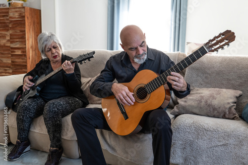 Couple, 70 years old, playing guitar on the sofa in their living room. Woman electric, Man, acoustic