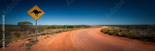 A banner with a road sign and a dirt road. A yellow sign with a black kangaroo silhouette designating the kangaroo transition zone. The road turns right and is surrounded by sparse vegetation. photo