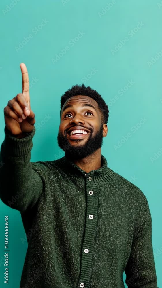 Smiling man points upward against a teal background Smiling man points upward against a teal background