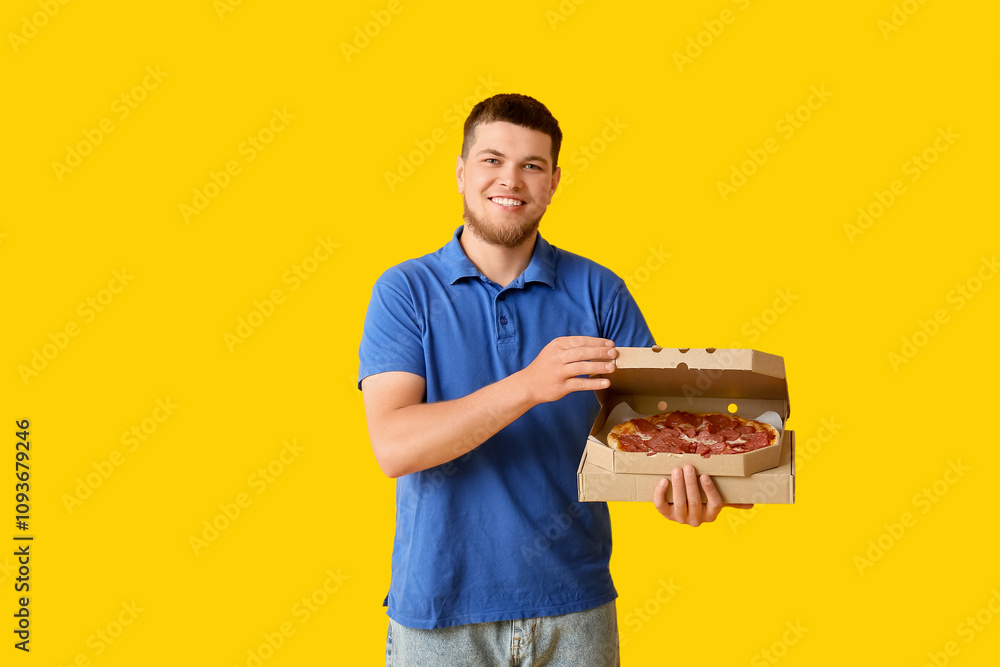 Happy young man holding cardboard box with tasty pepperoni pizza on yellow background Happy young man holding cardboard box with tasty pepperoni pizza on yellow background