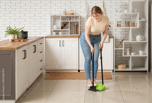 Foto Young woman sweeping floor in kitchen