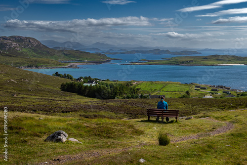 Single Woman On Bench Looks Over Atlantic Coast With Summer Isles, Isle Ristol And Eilean Mullagrach Near Village Altandhu In The Highlands Of Scotland, UK photo