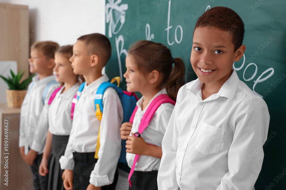 Little pupils with backpacks at blackboard in classroom Little pupils with backpacks at blackboard in classroom