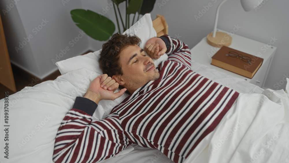 Young hispanic man stretches on bed in comfortable bedroom interior, exuding a relaxed and handsome demeanor in a cozy, indoor home setting. Young hispanic man stretches on bed in comfortable bedroom interior, exuding a relaxed and handsome demeanor in a cozy, indoor home setting.