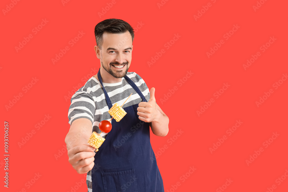 Young happy man with tasty fresh vegetables skewer showing thumb-up gesture on red background Young happy man with tasty fresh vegetables skewer showing thumb-up gesture on red background