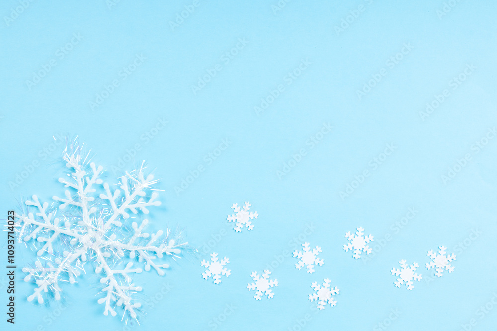 Close up pattern of white fake snowflakes. Christmas decoration over plain blue background, table top view, flat lay Close up pattern of white fake snowflakes. Christmas decoration over plain blue background, table top view, flat lay