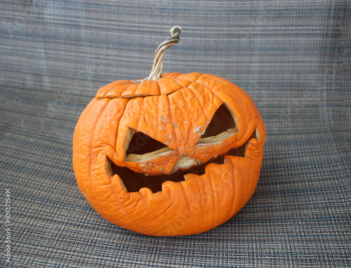 Wrinkled carved pumpkin with a spooky expression on a fabric background.