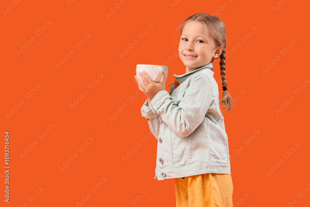 Cute little happy girl in autumn clothes with cup of tea on orange background Cute little happy girl in autumn clothes with cup of tea on orange background