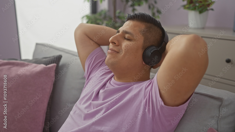 Relaxed hispanic man enjoying music on headphones in a cozy apartment living room. Relaxed hispanic man enjoying music on headphones in a cozy apartment living room.