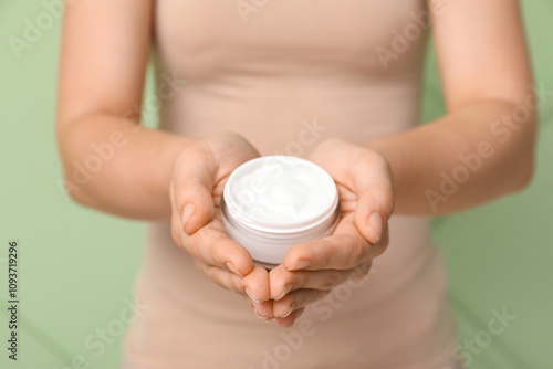 Young woman with jar of cosmetic cream on green background photo