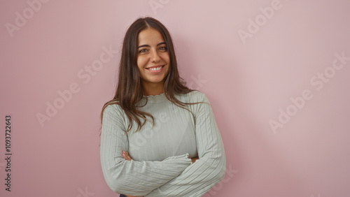 Woman smiling confidently with crossed arms against a pink wall, embodying a relaxed and approachable demeanor in a simple, elegant style.