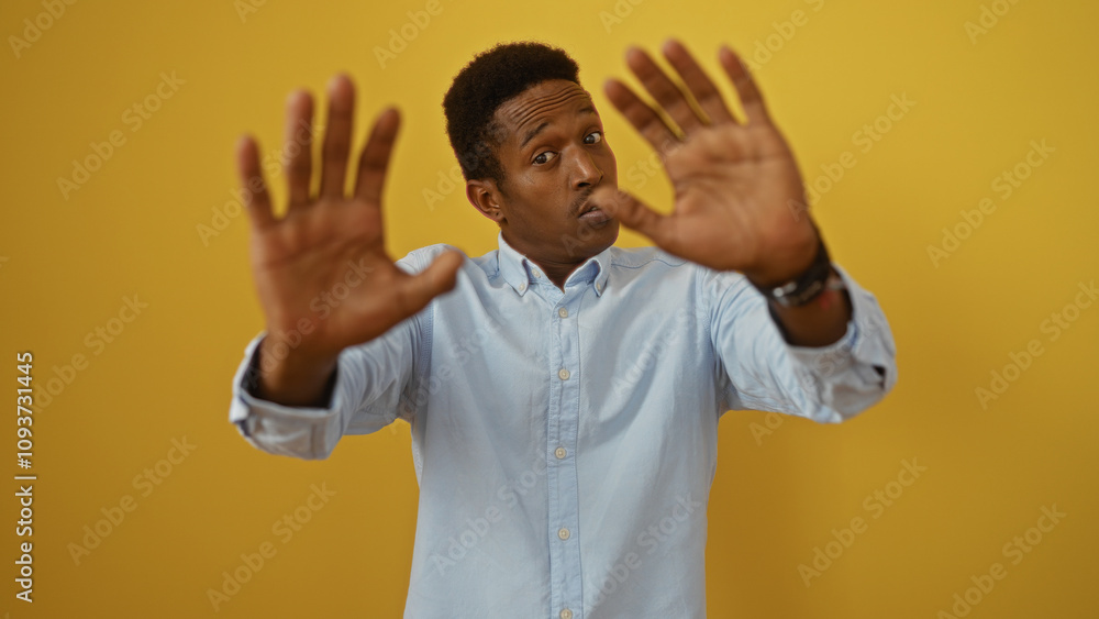Man making stop gesture over yellow background with outstretched hands wearing a blue shirt, capturing a sense of caution and communication. Man making stop gesture over yellow background with outstretched hands wearing a blue shirt, capturing a sense of caution and communication.