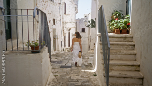 Photos A young, beautiful hispanic woman walks through the charming old town of ostuni in puglia, italy, surrounded by whitewashed buildings and cobblestone streets