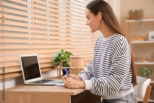 Young woman with ear plugs working near table at home