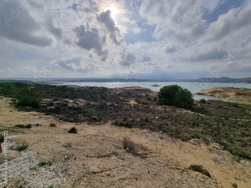 Stausee inmitten einer kargen Landschaft, umgeben von felsigen Hügeln. Ein beeindruckender Wolkenhimmel dominiert die Szenerie und verleiht ihr Dramatik photo