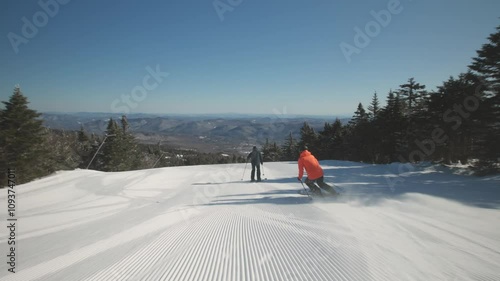 4K video of a couple man and woman skiers alpine skiing on cold winter snow at a ski resort mountain with sunshine. Adventure and thrill while on vacation and holiday. Killington, Vermont, USA. photo