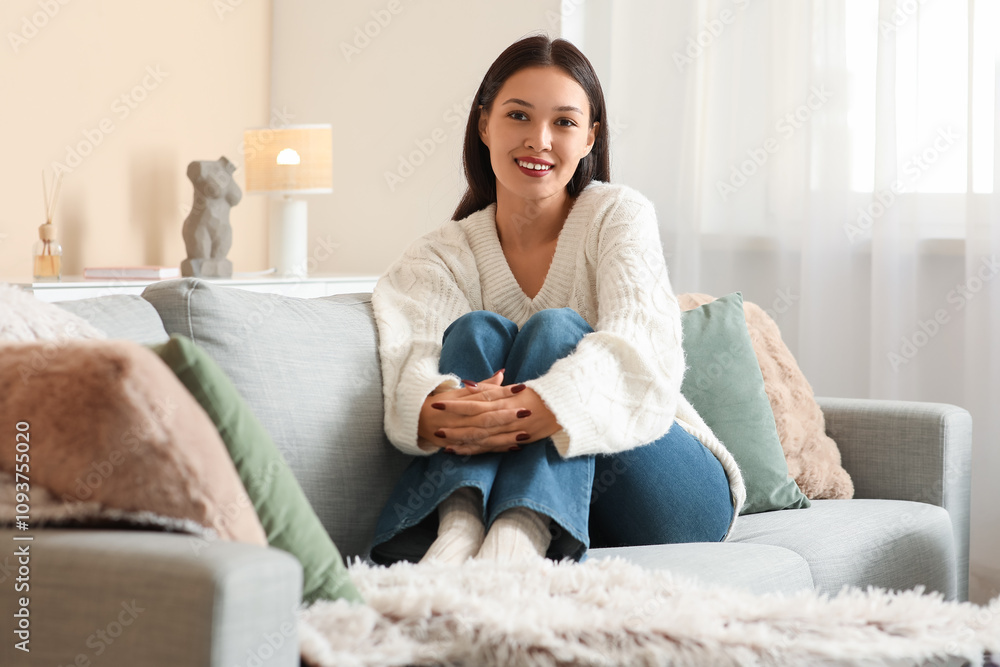 Beautiful young woman in white knitted sweater sitting on sofa at home Beautiful young woman in white knitted sweater sitting on sofa at home