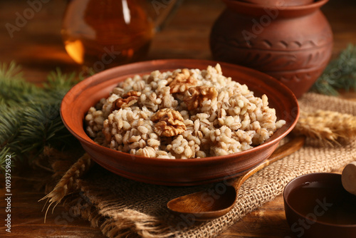 Bowl of traditional Ukrainian Kutya dish with sweet honey and fir branches on wooden background, closeup