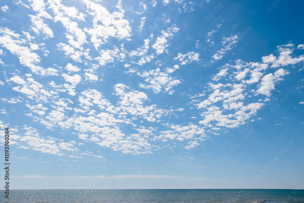 Obraz premium With a backdrop of blue sky, the fluffy clouds drift over a calm Lake Michigan on a morning in early June off the beach at Harrington Beach State Park, Belgium, Wisconsin