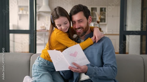 Smiling carefree Caucasian dad man parent reading card present from little daughter kid. Loving family male father guy hugging girl child touch at home Father's Day celebration gift parenting holiday