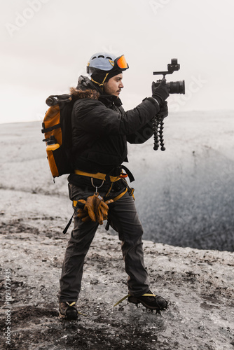 Content creator is recording video footage on a glacier using a gimbal and camera, wearing crampons for safety photo