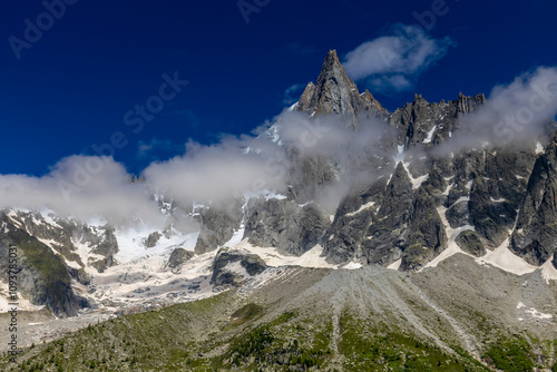 Petit Dru granite mountain wall and summit in Chamonix valley, french Alps. Prominent mountain peak in the Alps, stunning landscape view of the rocky peak covered with clouds, snow and ice