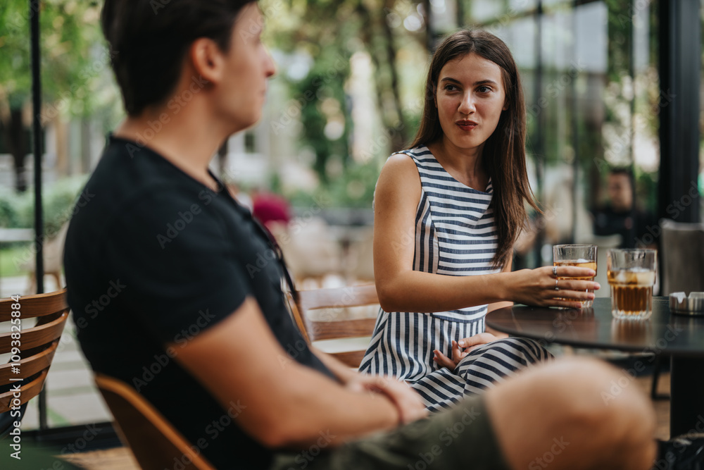 Two friends engaging in a casual conversation at an outdoor cafe. The woman, holding a drink, listens attentively. The ambiance is relaxed and friendly, perfect for social interactions. Two friends engaging in a casual conversation at an outdoor cafe. The woman, holding a drink, listens attentively. The ambiance is relaxed and friendly, perfect for social interactions.