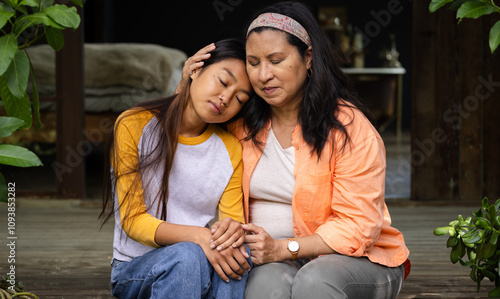 Grandmother and asian female teenager sharing heartfelt moment on porch, embracing and comforting photo