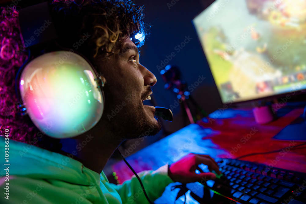 Photo of handsome young man excited cheerful smile sit table play gamer computer game late night blue purple indoors house late neon light Photo of handsome young man excited cheerful smile sit table play gamer computer game late night blue purple indoors house late neon light