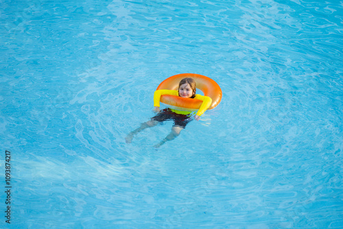 Child play in pool on inflatable ring. Kid with inflatable ring in swimming pool. Child water toys. Children play in tropical resort. Child playing in swimming pool. Summer vacation concept.