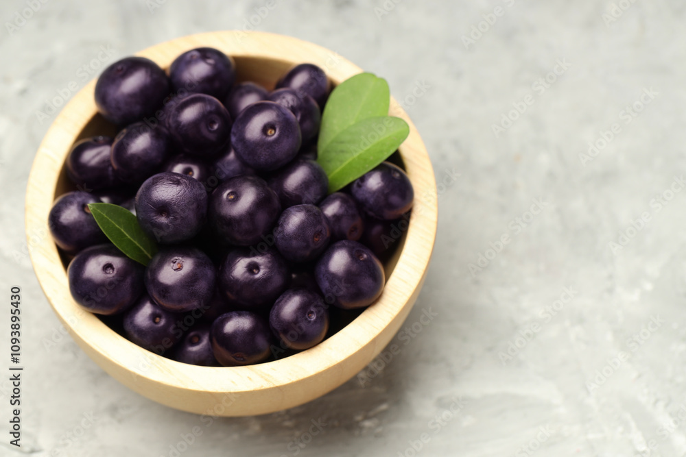Ripe acai berries and leaves in bowl on grey textured table, closeup. Space for text Ripe acai berries and leaves in bowl on grey textured table, closeup. Space for text