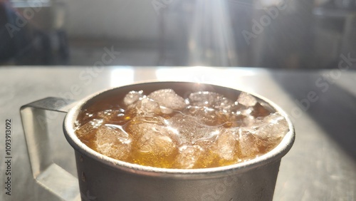 Ice cube is floating on brown iced tea with morning sunlight