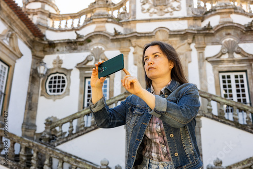 Young adult woman tourist standing near Mateus Palace at Vila Real, Portugal, and taking photo or video using smartphone photo