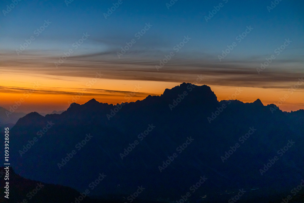 Sunset in the mountains. Red and orange burning sky horizon behind the alpine mountain range. Rocky mountain peaks of the Dolomites at sunset and dawn at sunrise light sunrays going through the clouds Sunset in the mountains. Red and orange burning sky horizon behind the alpine mountain range. Rocky mountain peaks of the Dolomites at sunset and dawn at sunrise light sunrays going through the clouds