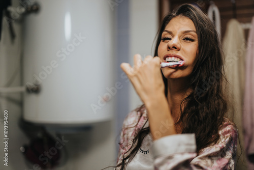 A woman begins her day with a cheerful smile as she brushes her teeth, embodying a healthy morning routine in a cozy bathroom setting. photo