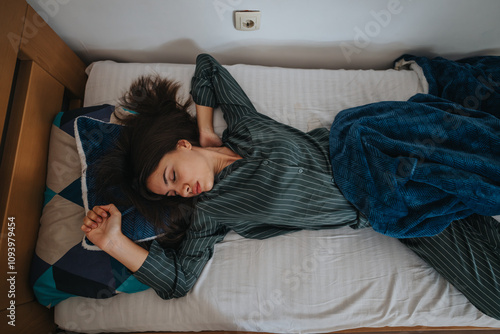 Billede på lærred A relaxed woman sleeping comfortably on a bed, wrapped in a blue blanket