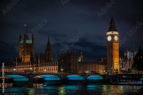 Big Ben and the Houses of Parliament illuminated at night, viewed from the Thames River, iconic Westminster Bridge glows with vibrant lights, architectural beauty of London, England, UK (October 2024)
