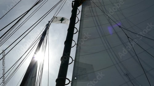 Maine state flag waving with sails on sailboat and sun peeking behind mast