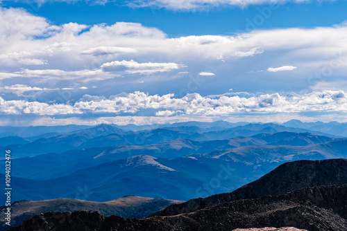 Expansive mountain view during midday with blue skies and layered peaks under a dramatic cloudscape in a remote wilderness area